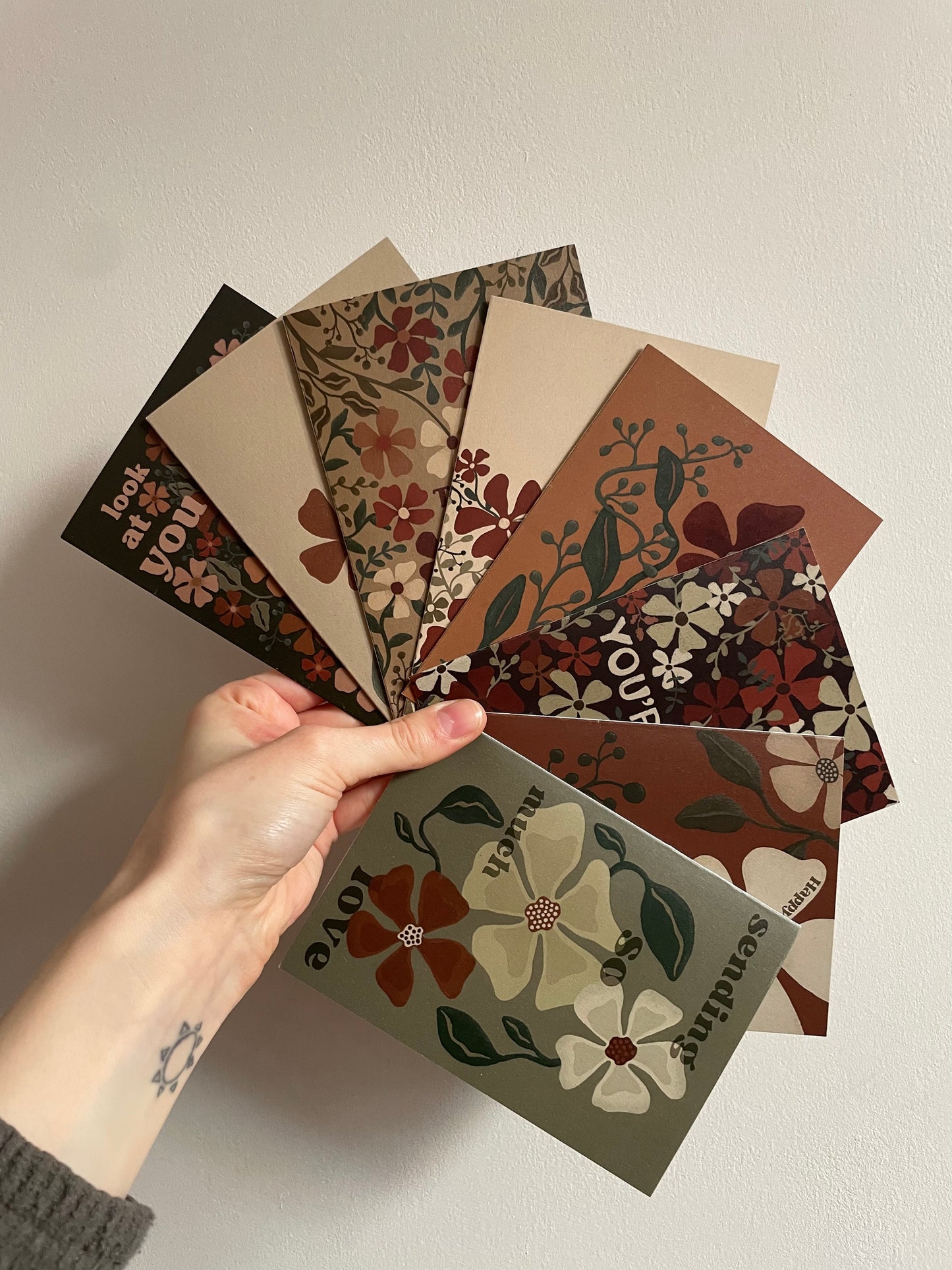 A hand holds 8 greetings cards, designed with bold floral designs.